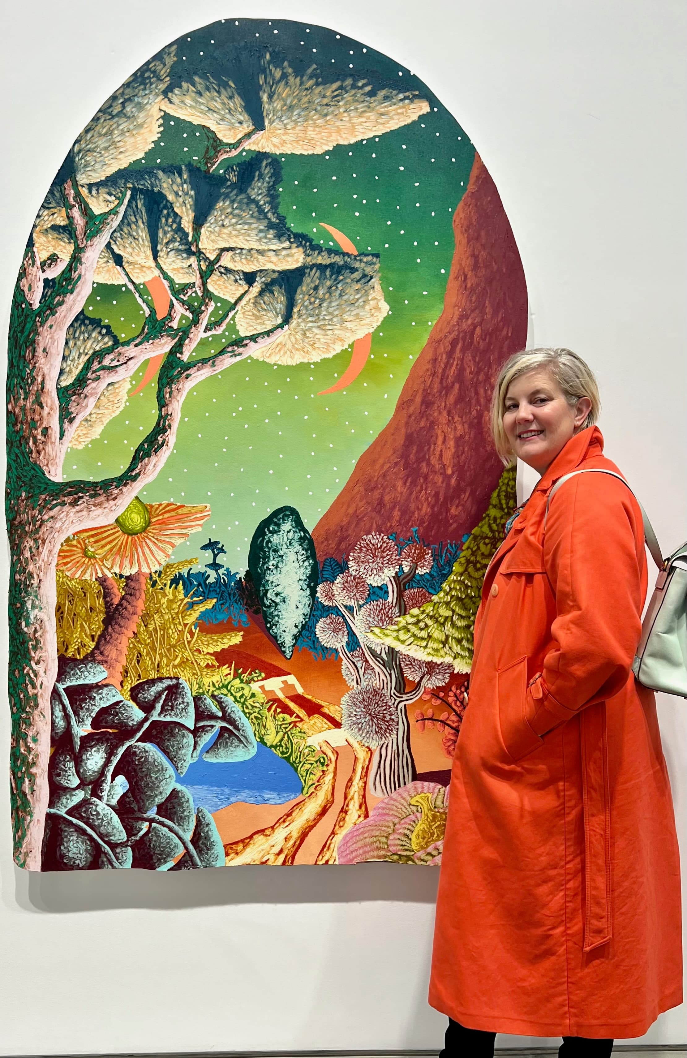 Skye Howell Henley beside a large colorful landscape painting